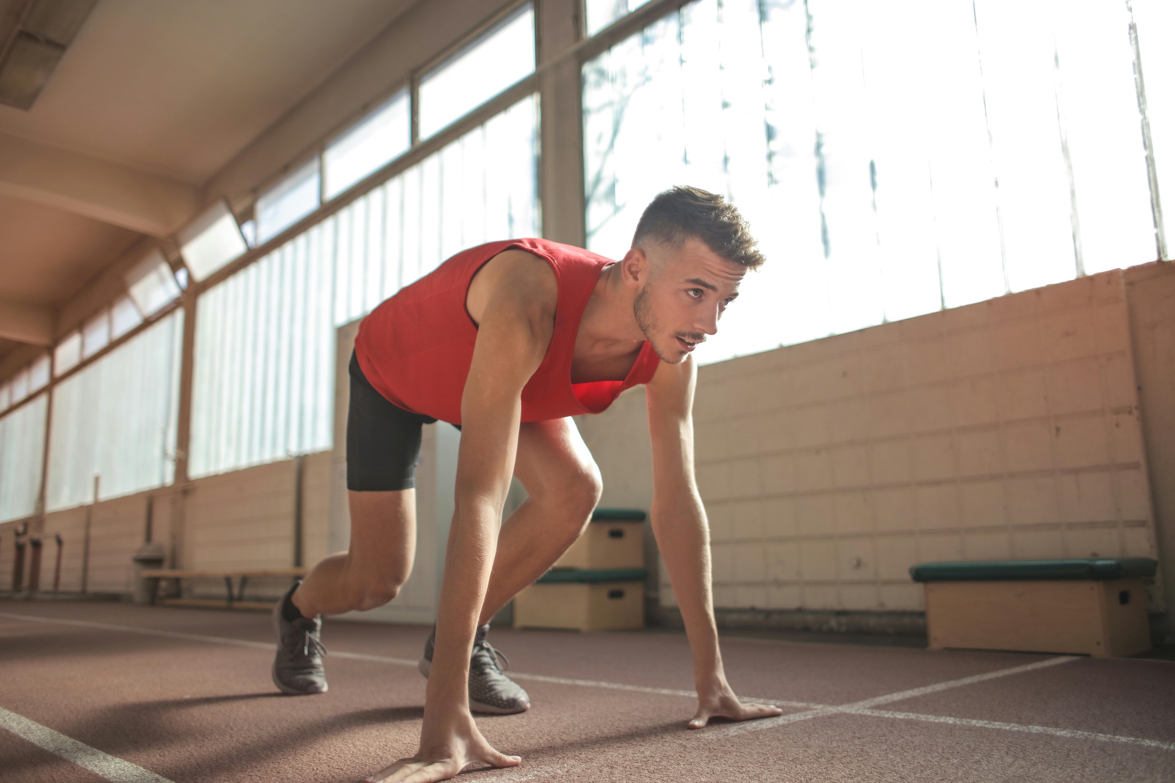 Runner in red tank top set on indoor track about to run