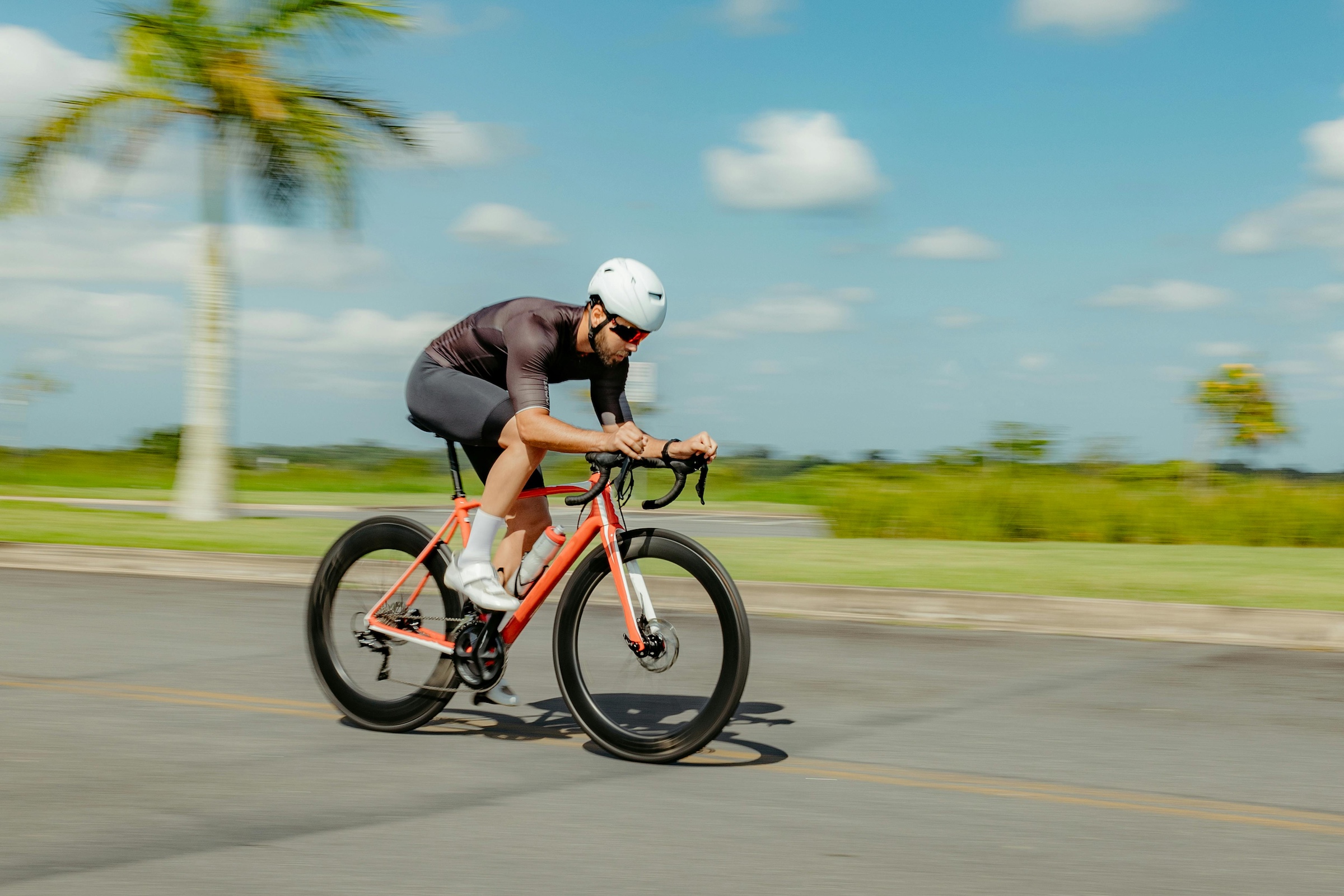 Man riding bike at top speed on a road with palm trees