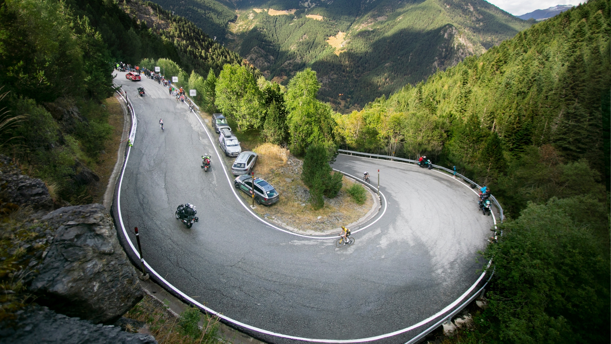 Wide shot of a cyclist rounding a paved mountain switchback
