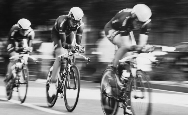 Black and white photo of three cyclists gaining speed in race