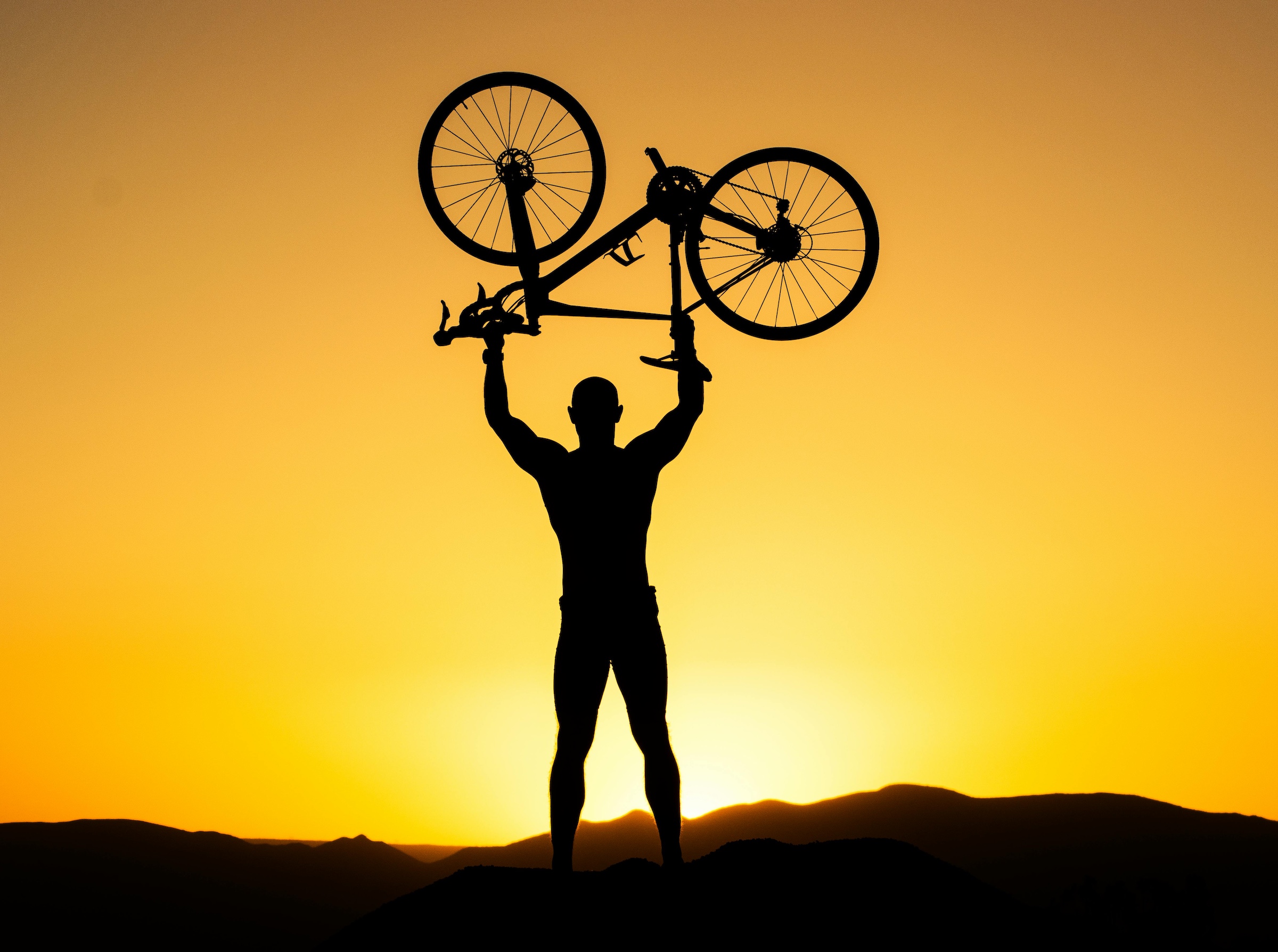 Cyclist holding bike in air in front of sunset for training and performance goals