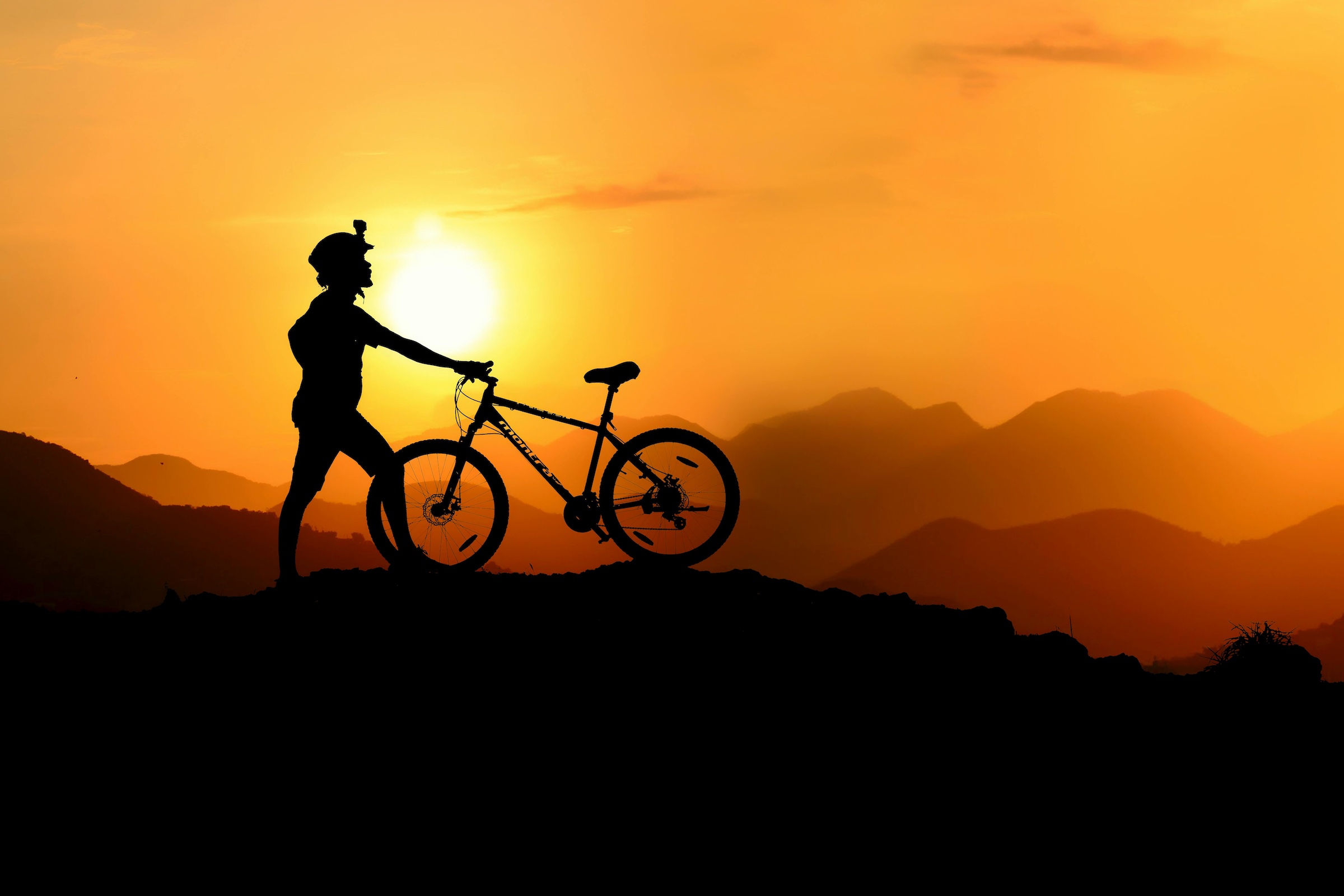 Mountain Biker at the peak in front of sunset for MTB fit and strength