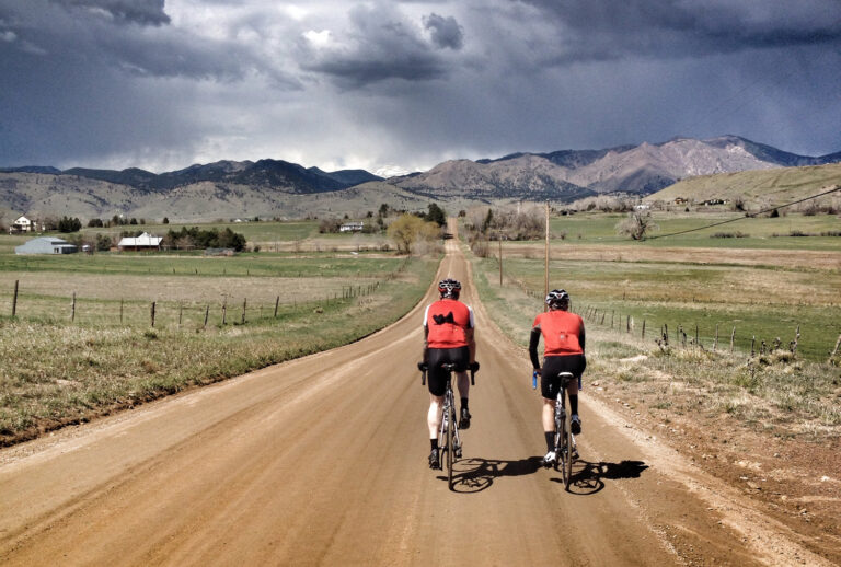Two cyclists wearing red jerseys ride into the distance on dirt roads in North Boulder, Colorado. Cycling base training and LSD long-slow distance ride.