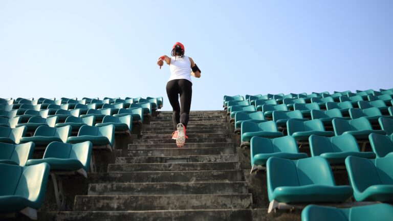 Rear view of a woman running up stairs at an outdoor stadium